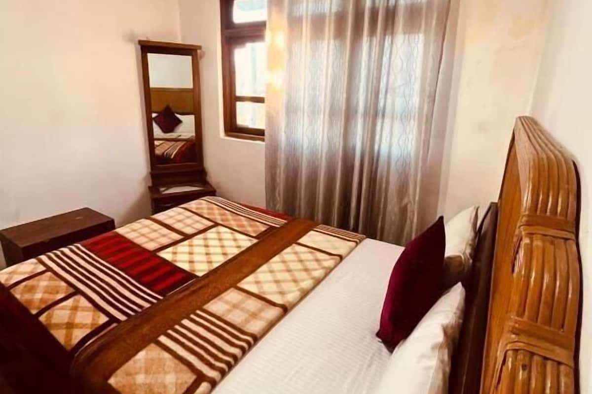 A bedroom with a bed, a wooden headboard, a nightstand, a mirror, and a window with curtains.