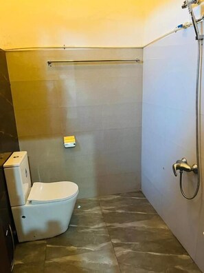 A small, modern bathroom with a toilet, a shower, and a hand dryer. - The Budget White House Nuwaraelliya (Nuwara Eliya)