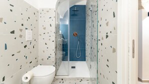 Un baño moderno con ducha de vidrio, inodoro y un rollo de papel higiénico en el suelo.