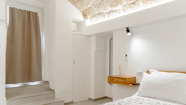 Un dormitorio con cama, mesita de noche, espejo y ventana con cortina.