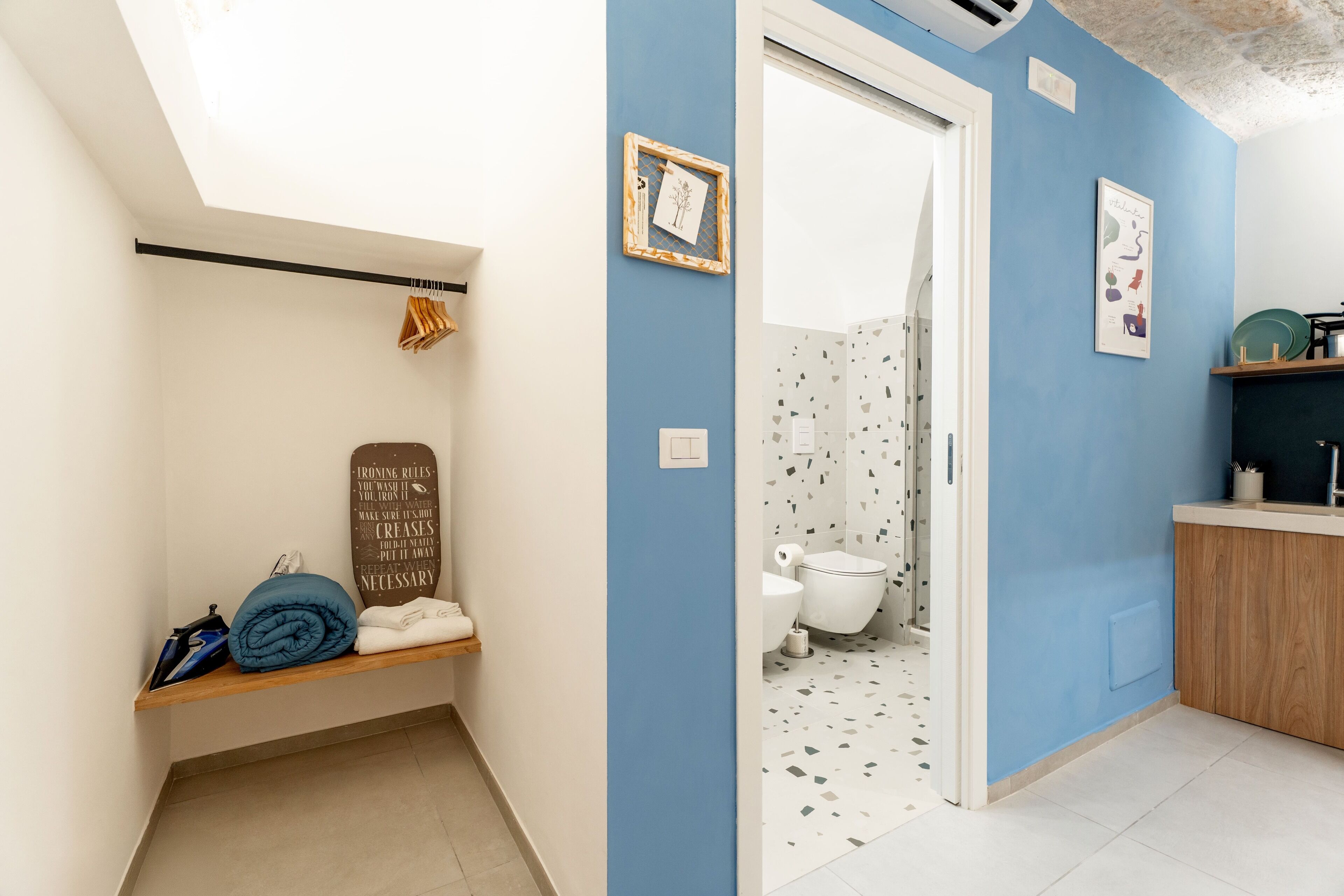 Ein Badezimmer mit blauer Wand, einer weißen Toilette, einer Duschkabine und einem Regal mit Handtüchern und einer zusammengefalteten Decke.