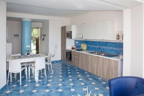 Egy modern konyha központi szigettel, étkezővel, székekkel és kék csempékkel burkolt padlóval.