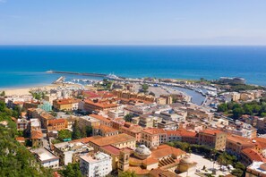 A coastal cityscape with historic buildings, a marina, and a pier extending into the sea. - Villa Fortunata (Terracina)