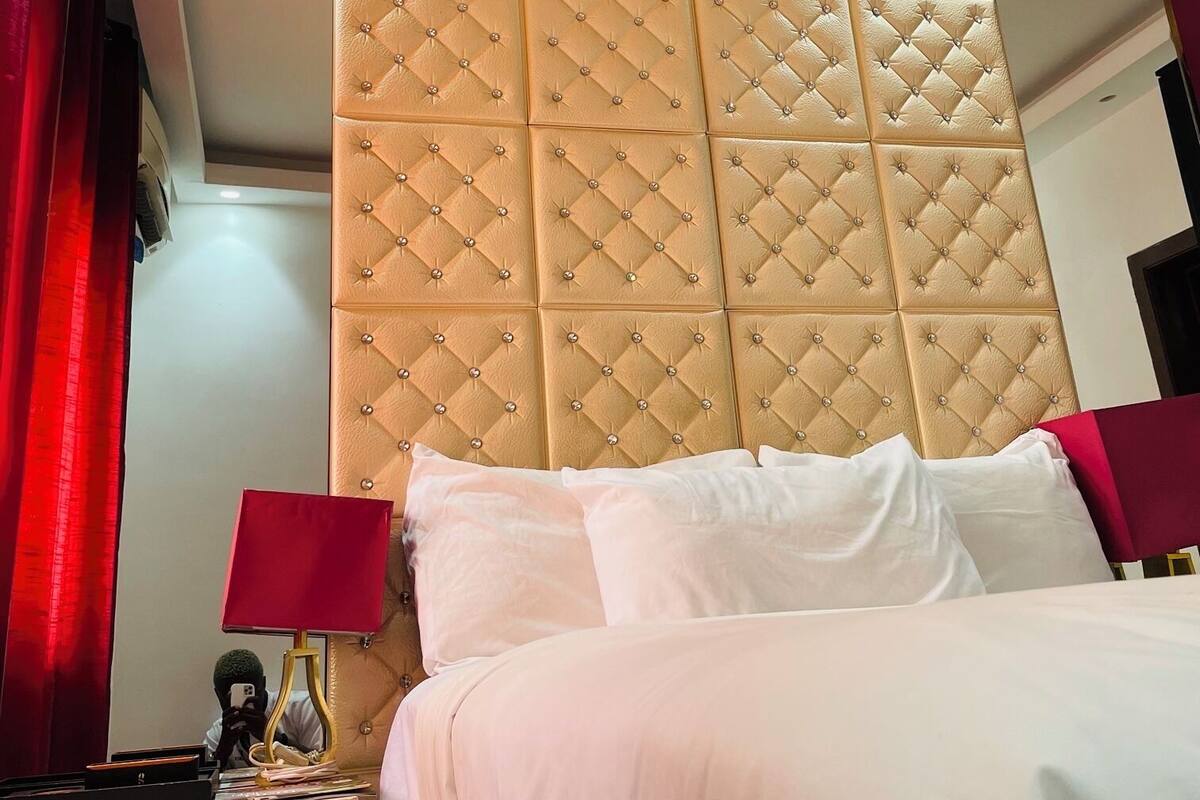 A hotel room with a tufted headboard, a bed with white linens, a nightstand with a lamp, and a mirror.