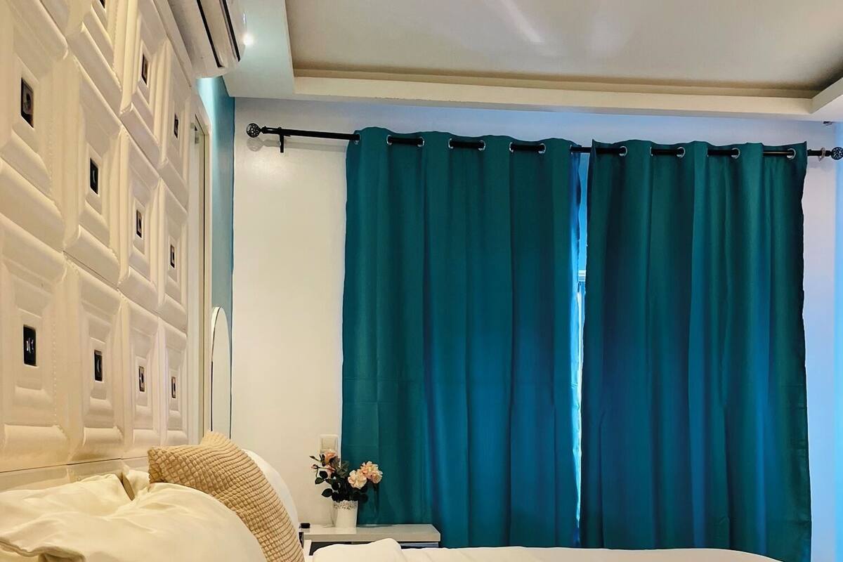 A hotel room with a bed, a nightstand, a vase with flowers, and teal curtains.