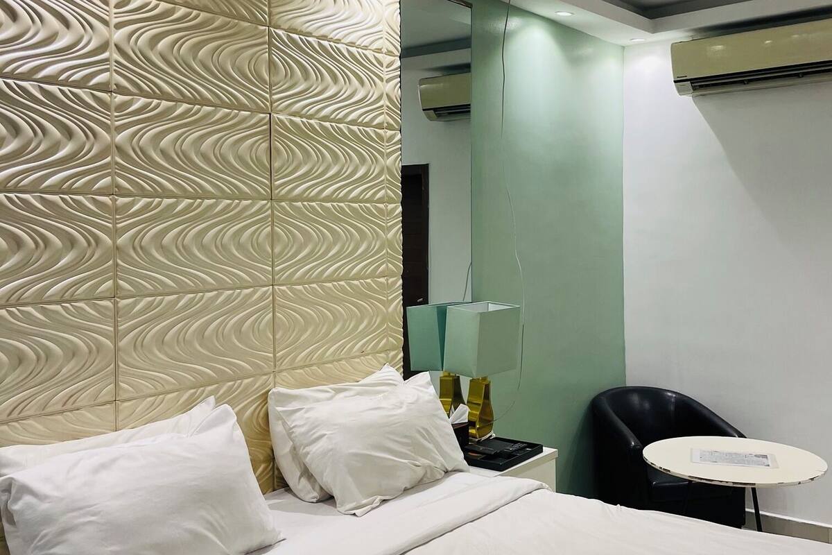 A hotel room with a bed, a nightstand, a lamp, a chair, and a small table.
