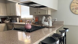 Une cuisine avec un plan de travail en granit, une bouilloire rose, une bouilloire blanche et une horloge au mur.