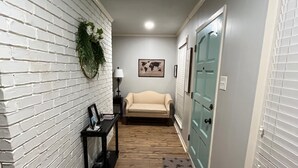 Un couloir avec un mur en briques, un plancher en bois, un canapé, une table avec une lampe et une porte avec une fenêtre.
