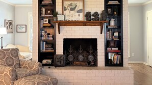 Un salon doté d’une cheminée, de bibliothèques, d’un fauteuil à motifs et d’un ventilateur de plafond.