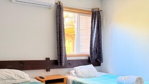 Una habitación con dos camas, piso de madera, ventana con cortinas y aire acondicionado.