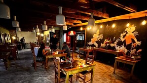 Un restaurante con mesas y sillas de madera, lámparas colgantes y un mural en la pared.
