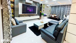 A modern living room with a flat-screen TV, grey sofas, a coffee table, and a dining area with a table and chairs. - Alubarika Service Apartments (Lagos)