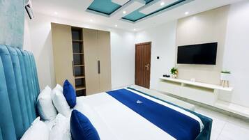 Un dormitorio moderno con cama, armario, televisor y una planta pequeña.