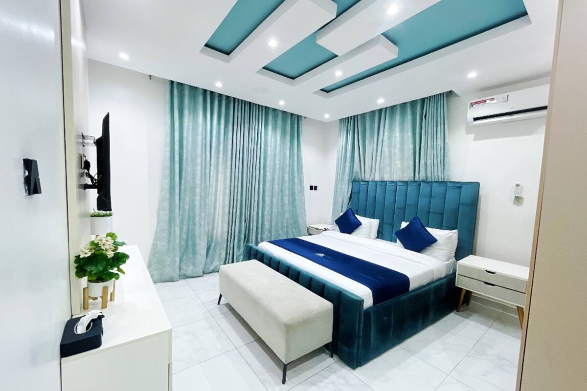 A modern bedroom with a large bed, a bedside table, a bench, and a small desk.