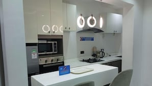 A modern kitchen with white cabinets, a microwave, an oven, and a gas stove. There are two chairs at a table with a sign indicating a no-smoking policy. - Alubarika Service Apartments (Lagos)