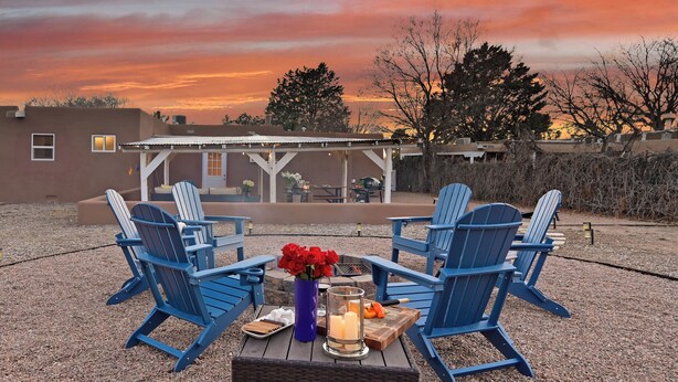 A patio with Adirondack chairs, a table with candles, and a vase of red flowers. - Private Santa Fe Retreat Near Plaza · Fire Pit · 3 King Bedrooms (Santa Fe)