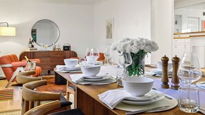 A dining area with a wooden table set for a meal, white chairs, a vase with white flowers, and a kitchen in the background. - Private Santa Fe Retreat Near Plaza · Fire Pit · 3 King Bedrooms (Santa Fe)
