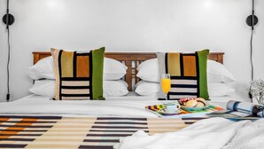 A neatly made bed with a striped blanket, a bedside table with a glass of orange juice, a plate of food, and a rolled-up towel. - Private Santa Fe Retreat Near Plaza · Fire Pit · 3 King Bedrooms (Santa Fe)