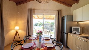 A dining area with a table set for four, a kitchen with a refrigerator and a microwave, and a view of the outdoors through a glass door. - Sardinia Luxury Villa with Pool, Botanical Park and Fast Wi-Fi  (Sardegna)