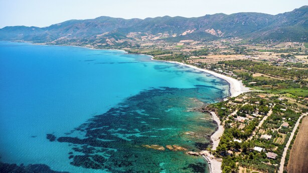 An aerial view of a coastal area with clear blue waters, a sandy beach, and a backdrop of green hills. - Sardinia Luxury Villa with Pool, Botanical Park and Fast Wi-Fi  (Sardegna)