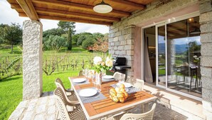 An outdoor patio with a wooden table set for dining, stone pillars, and a view of a vineyard. - Sardinia Luxury Villa with Pool, Botanical Park and Fast Wi-Fi  (Sardegna)