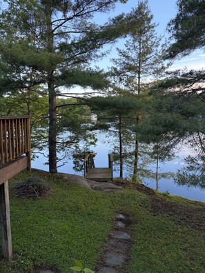 A wooden deck leading to a dock over a calm lake, surrounded by tall pine trees.