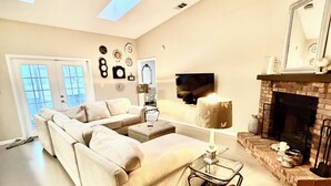 A spacious living room with a large sofa, a small table, a fireplace, and a ceiling fan.