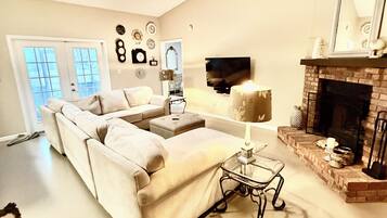 A spacious living room with a large sofa, a small table, a fireplace, and a ceiling fan.