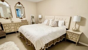 A bedroom with a large bed, two nightstands, a dresser, a ceiling fan, and two wall mirrors.