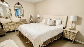 A bedroom with a large bed, two nightstands, a dresser, a ceiling fan, and two wall mirrors.