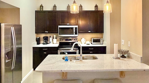 A modern kitchen with dark cabinets, stainless steel appliances, a central island with stools, pendant lighting, and a skylight.