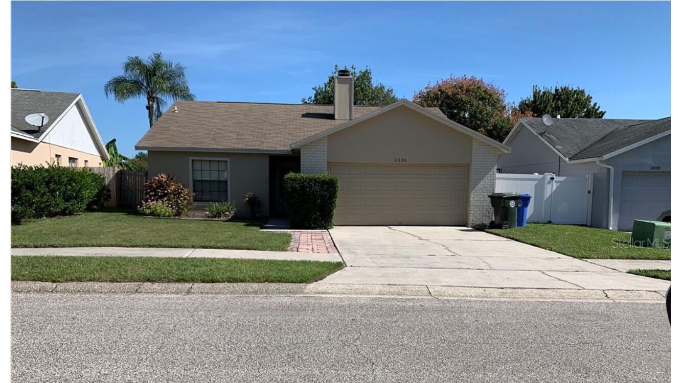 A single-story house with a garage, a front yard with a lawn and a small garden, and a clear sky.
