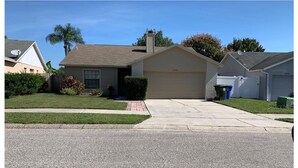 A single-story house with a garage, a front yard with a lawn and a small garden, and a clear sky.