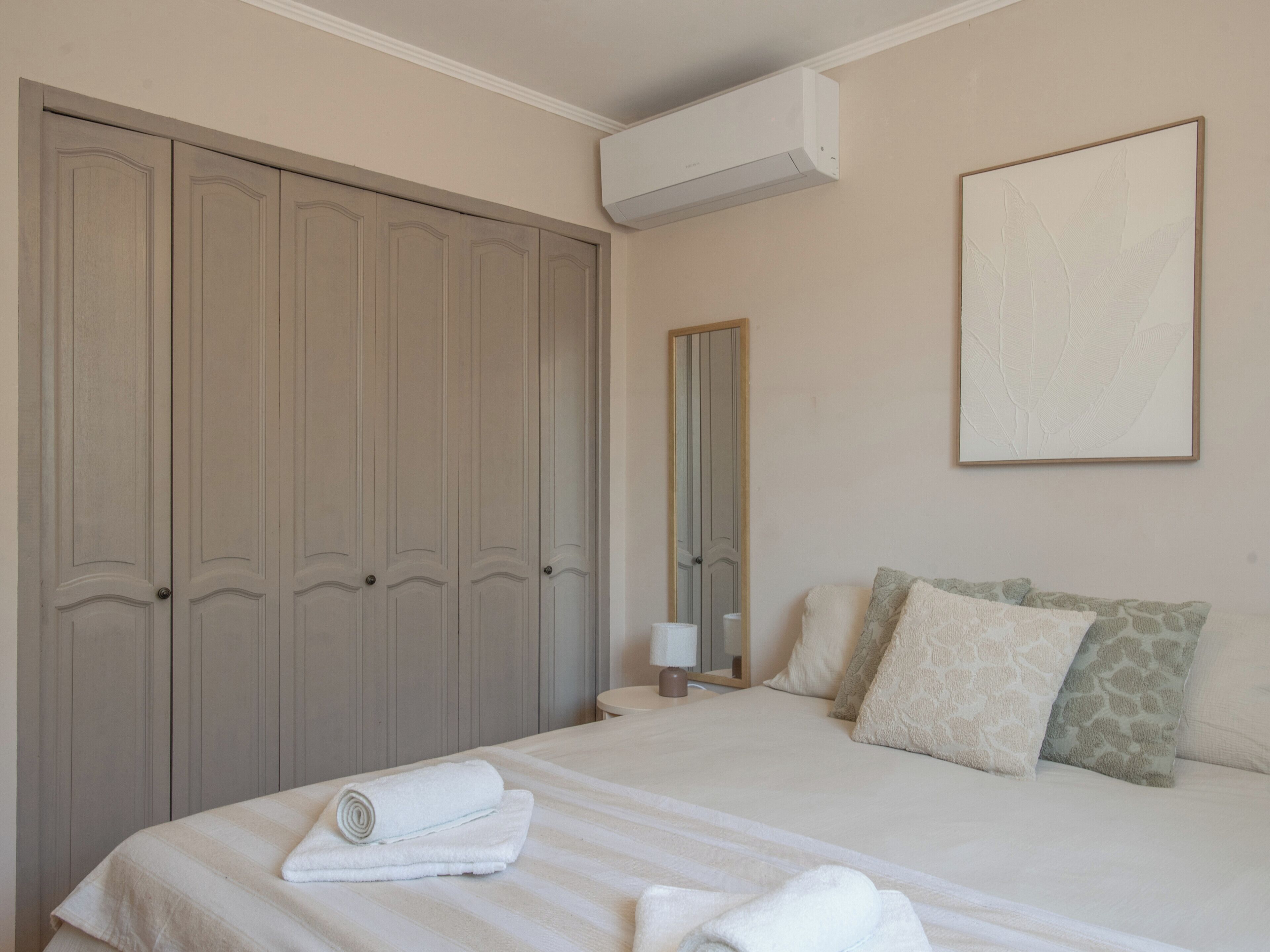 A bedroom with a bed, a wardrobe, a mirror, and a wall-mounted air conditioner.