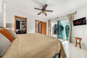 Ein Schlafzimmer mit Bett, Deckenventilator, Fernseher und Blick ins Freie.