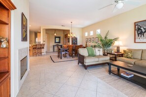 A spacious living room with a fireplace, dining area, and a ceiling fan.