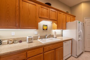 A kitchen with wooden cabinets, a white countertop, a sink, a toaster, a dish soap dispenser, a paper towel holder, a refrigerator, and a dishwasher.