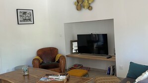 A living room with a television, a brown leather armchair, a white sofa, a wooden coffee table, and a decorative wall piece. - Charming family home in the heart of Périgord Noir, between Lascaux and Sarlat. (La Chapelle-Aubareil)