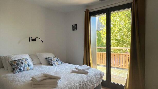 A bedroom with a bed, pillows, a headboard, a window with curtains, and a view of a balcony. - Charming family home in the heart of Périgord Noir, between Lascaux and Sarlat. (La Chapelle-Aubareil)
