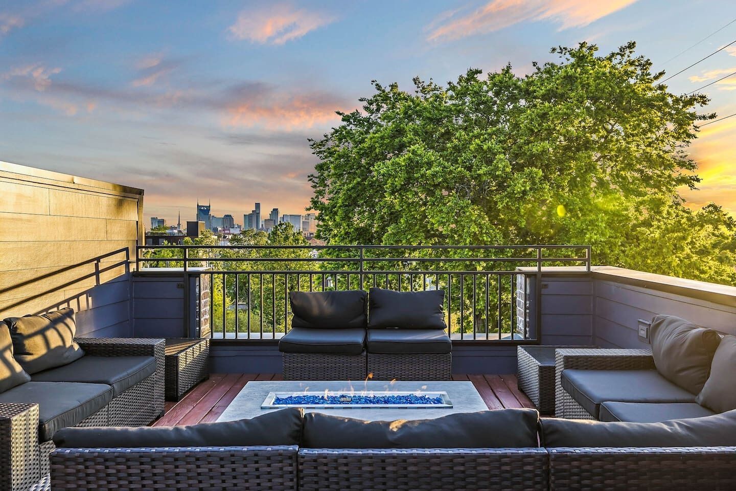 A rooftop terrace with wicker furniture, a fire feature, and a city skyline view.