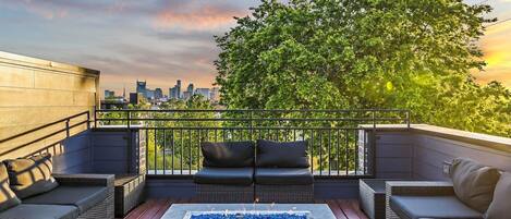 Terraza en la azotea con mobiliario de mimbre, una chimenea y vista al horizonte de la ciudad.