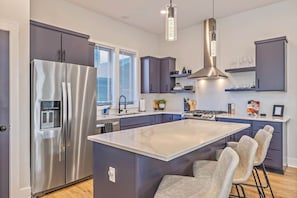 A modern kitchen with a stainless steel refrigerator, a central island with bar stools, and a gas stove. - 12 Rooms, 12 baths, 3 Townhomes. 2mi to Broadway (Nashville)