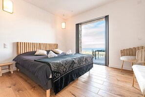 A bedroom with a large bed, a wooden headboard, a view of the sea through a glass door, and a chair by the window. - Villa Evasione - Climatisée, piscine vue mer (Santa-Reparata-di-Balagna)