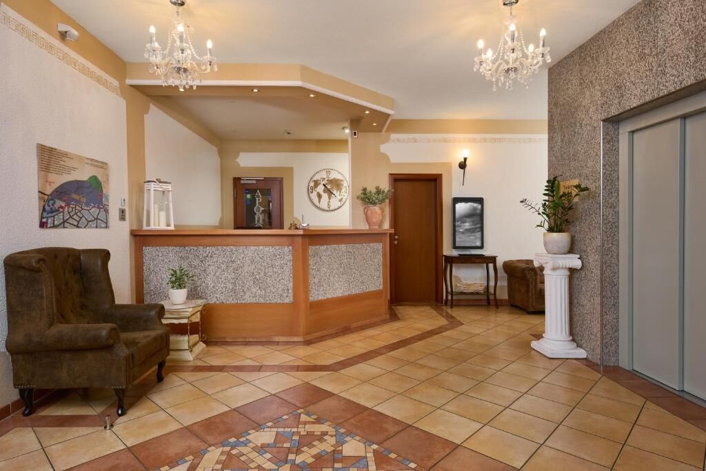 Un hall d’entrée avec un comptoir de réception, un fauteuil en cuir marron, un tapis à motifs et un lustre.
