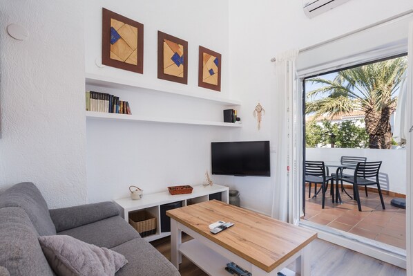 Una sala de estar con un sofá, una mesa de centro, un televisor y una estantería.