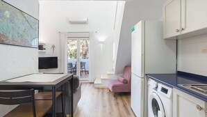 A compact kitchen with a washing machine, a dining area with a table and chairs, and a view through a door to an outdoor seating area. - Holiday Home 'Denia Encantadora' with Shared Pool, Wi-Fi and Air Conditioning (DENIA)