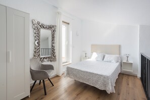 Un dormitorio con cama, una silla, cómoda, espejo y mesita de noche.