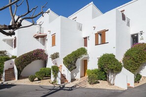 Una hilera de edificios blancos con balcones, una escalera y pequeños árboles.