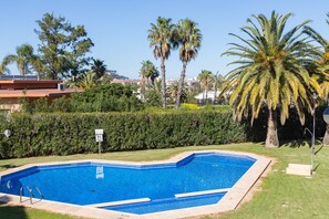 A swimming pool with a clear blue water, surrounded by a well-maintained lawn and palm trees. - Holiday Home 'Denia Encantadora' with Shared Pool, Wi-Fi and Air Conditioning (DENIA)