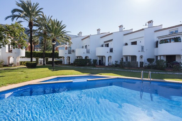 A swimming pool with a clear blue water surface, surrounded by white buildings with balconies and palm trees. - Holiday Home 'Denia Encantadora' with Shared Pool, Wi-Fi and Air Conditioning (DENIA)